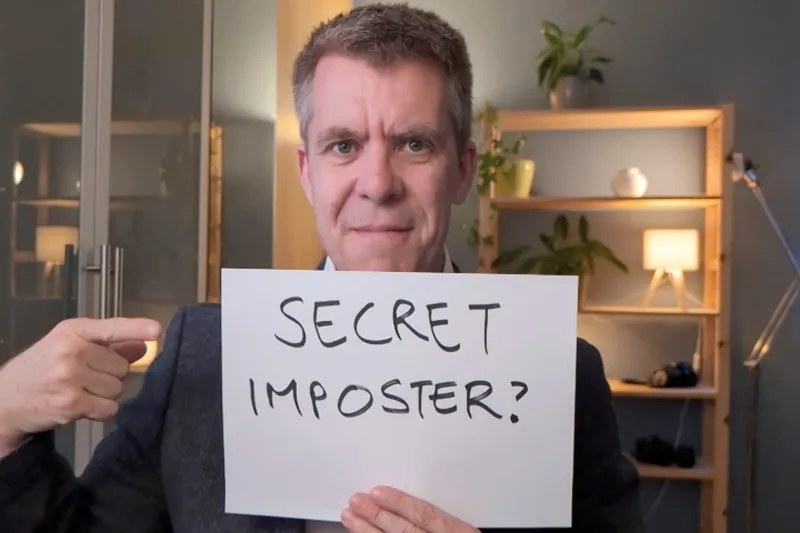 Benjamin Mitchell holding a sign saying - secret imposter?